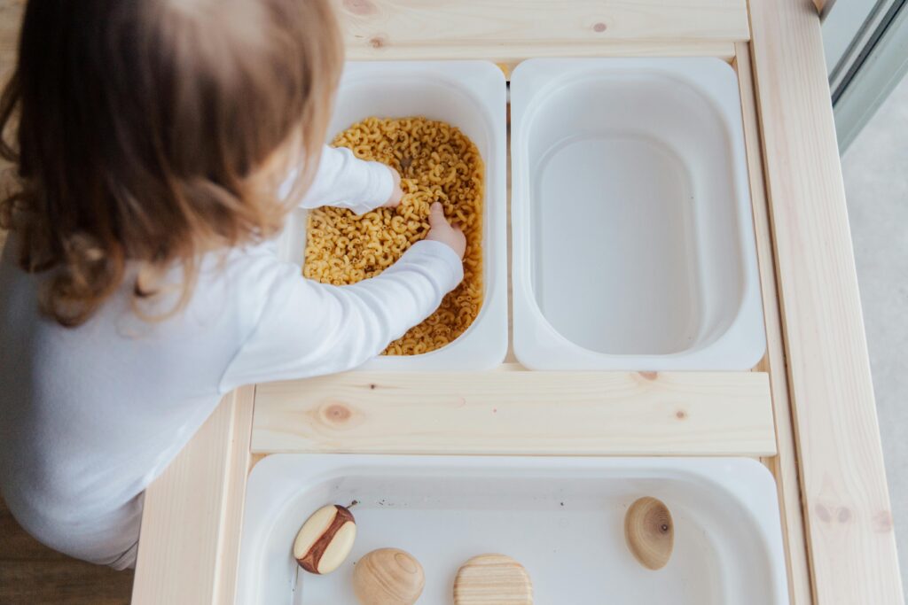 Curious autistic child engaging in sensory play with pasta, exploring textures indoors.