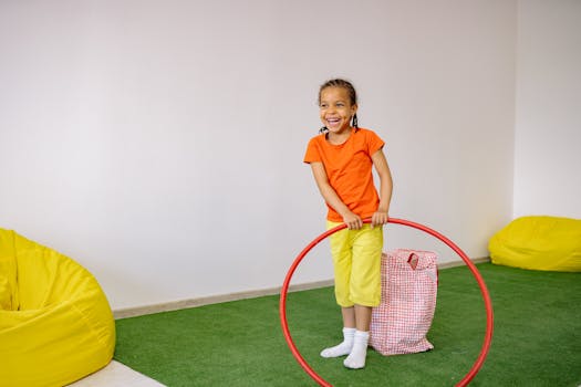 A smiling girl enjoys playing with a hula hoop indoors, surrounded by bean bags.